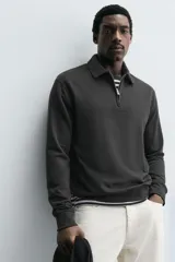 Polo de manga larga color gris oscuro, con diseño de textura estructurada, cuello solapa y cierre frontal de cremallera corta. Cuenta con puños y cintura de rib elástico.