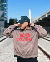 Campera negra con capucha y cierre frontal, con estampado del logo Rona Studio en color naranja en el pecho.