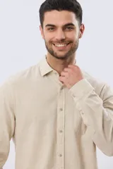 Camisa de lino de manga larga en color beige, con cuello camisero, cierre frontal de botones y un bolsillo ojal en el pecho.