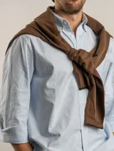 Camisa de corte regular confeccionada en algodón, con diseño de rayas verticales en tonos azul y blanco. Presenta cuello con botones, cierre frontal abotonado, bolsillo en el pecho con logo bordado y mangas largas.