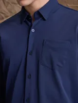 Camisa de manga larga color azul marino, con cuello clásico, cierre frontal de botones y un bolsillo en el pecho.