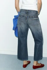 Jeans de tiro medio con corte cropped, confeccionados en denim azul con efecto lavado. Presentan trabillas en la cintura, cierre frontal con cremallera y botón metálico, bolsillos delanteros y traseros, y costuras laterales decorativas.