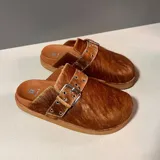 Mules de pelo color marrón con una tira en el empeine decorada con hebilla metálica grande y ojales metálicos.