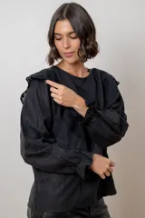 Blusa blanca de algodón con cuello redondo, mangas largas con puños elásticos y volados decorativos en los hombros.