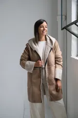 Tapado tipo gamuza con interior de corderito sintético, color beige con detalles en crudo. Presenta capucha, cierre frontal completo y puños con vuelta de corderito.