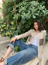 Camisa color beige con botones, de mangas largas y dos bolsillos frontales con solapa de cuero sintético color plateado.