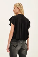 Camisa negra de viscosa con cuello redondo, cierre frontal con cordones y mangas cortas con volados. Presenta detalles de frunces en el pecho y hombros.