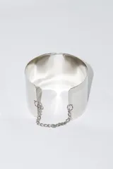 Brazalete rígido plateado con cadena de seguridad.