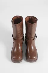 Botas de caña media color marrón, elaboradas en cuero vegano, con diseño estilo biker, taco bajo, hebillas metálicas decorativas y argollas laterales.