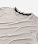Remera deportiva de hombre con tecnología dry fit, cuello redondo y manga corta. Presenta un diseño liso en color beige con una pequeña etiqueta decorativa en el dobladillo.
