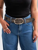 Cinto de cuero marrón con efecto desgastado, hebilla metálica ovalada grande y detalles de tachas y apliques decorativos.