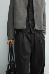 Pantalón negro de corte relaxed fit y estilo wide leg, con pliegues frontales dobles, bolsillos delanteros y detalle de bolsillos traseros de vivo. Cierre frontal cruzado con cremallera y gancho metálico oculto.