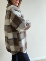 Sobrecamisa de paño con diseño a cuadros en tonos marrones, grises y blancos. Presenta cuello clásico, cierre frontal con botones y bolsillos delanteros con tapa.