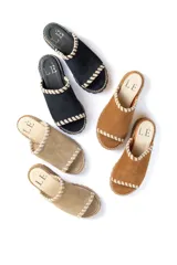 Chancla tipo mule de gamuza color beige, con puntera abierta y suela track gruesa. Presenta pespuntes decorativos en color claro alrededor del borde superior y en la unión de la capellada con la suela.