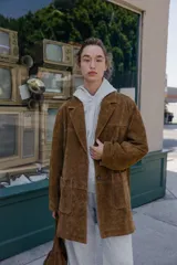 Chaqueta larga de piel color marrón, con cuello solapa, manga larga, bolsillos delanteros de plastrón y cierre frontal con botones.