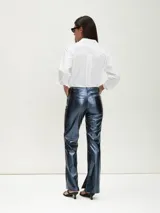 Pantalón de tiro alto, corte recto y ligeramente acampanado en la parte inferior, color azul oscuro metálico con acabado brillante. Presenta costuras visibles en el frente de las piernas y aberturas en los tobillos.