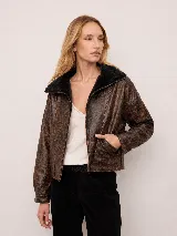 Chaqueta estilo bomber de cuero con acabado rústico y efecto desgastado. Presenta un diseño amplio con mangas caídas, largo a la cintura y cuello con aplique de corderito.