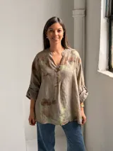 Blusa de lino color visón con estampado botánico en tonos marrones y verdes, cuello en V con abertura y un botón grande decorativo. Tiene mangas largas con tirilla para sujetar arremangadas y corte holgado.