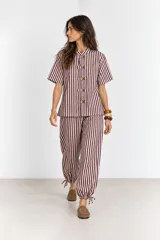 Pantalón de algodón a rayas borra de vino y blancas, de corte holgado estilo globo con cintura elástica, bolsillos laterales y detalle de ajuste con cordón en los tobillos.