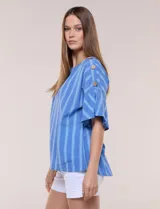 Blusa de corte cuadrado y silueta amplia, color azul con diseño de rayas verticales en tonos más claros. Cuenta con cuello redondo y mangas cortas acampanadas, decoradas con una hilera de botones de madera sobre los hombros.