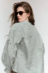 Blusa de escote pico y manga larga con puño elástico y volante. Presenta un diseño de rayas verticales finas en azul claro y blanco, con flores en relieve.