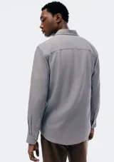 Camisa de manga larga en color gris, con cuello clásico, cierre frontal de botones y un bolsillo en el pecho.