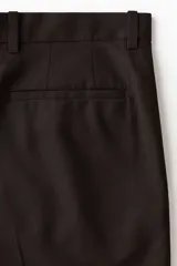 Bermuda de sarga color marrón oscuro, de corte holgado, con bolsillos laterales y traseros, y cierre frontal oculto con botones.
