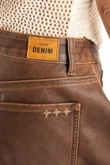 Bermuda de cuero vegano color marrón, con corte wide leg y tiro medio. Presenta diseño de cinco bolsillos y cierre frontal con botón metálico.