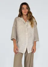 Camisa de corte oversize y diseño holgado, con cuello clásico, cierre frontal de botones y mangas tres cuartos.