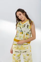 Chaleco de lana merino color crema, con escote en V y diseño sin mangas. Se usa sobre una camisa mostaza de mangas largas con puños elásticos.