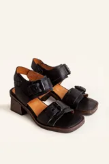 Sandalias de cuero negro con taco bloque de madera tallada, tiras con hebillas grandes y punta cuadrada.