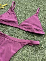 Conjunto de bikini color uva metalizado, compuesto por un corpiño triangular fijo con abertura para tazas soft y una bombacha colaless regulable.