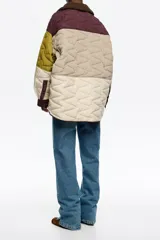 Abrigo acolchado de corte recto con diseño patchwork en tonos burdeos, beige y verde oliva. Presenta cuello camisero de pana, cierre frontal con botones de presión, bolsillos de tapeta en el bajo y bolsillos de vivo en el pecho.