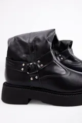 Bota de caña alta confeccionada en cuero vacuno color negro, con suela track de plataforma y detalle de tira con argolla metálica y tachas en el tobillo.