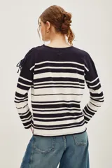 Remera de manga larga a rayas horizontales en azul marino y blanco, con cuello redondo y detalle de parche bordado en forma de corazón con flecha en el pecho. Presenta lazos decorativos en los hombros.