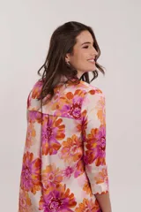 Vestido camisero midi con estampado floral en tonos naranja, rosa y fucsia. Tiene cuello camisero, mangas 3/4 y aberturas laterales.