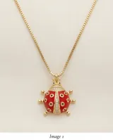Cadena de eslabones finos con baño de oro y dije en forma de mariquita esmaltada en color rojo, con detalles de circonias incrustadas.