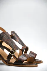 Sandalia de taco medio cuadrado, confeccionada en cuero con textura de piel de serpiente. Presenta un diseño de tiras cruzadas con hebillas metálicas ajustables y cierre de pulsera al tobillo.