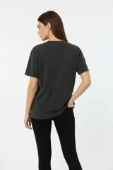 Remera de algodón, color gris oscuro con efecto gastado (acid wash), corte holgado y manga corta. Presenta un estampado frontal con motivos florales y texto en tonos rosados y blancos, incluyendo las frases "WILD ROSE ART", "ROSE POWER", "ST 1978" y "ROCKSTAR".