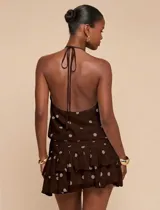 Vestido corto marrón con estampado de lunares beige, diseño sin mangas, cuello halter y falda con volantes escalonados.