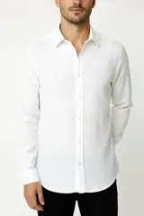 Camisa de algodón blanca, de manga larga, con cuello camisero y cierre frontal de botones.