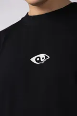 Remera negra de corte oversize con cuello redondo y estampa pequeña en el centro del pecho con forma de ojo que contiene un símbolo de yin y yang.
