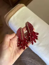 Par de aros colgantes color rojo con forma de abanico. Presentan una base con forma de gota y apliques de strass dorados.