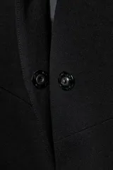 Blazer entallado negro con cuello sin solapa, manga larga y bolsillos de vivo en el delantero. Cuenta con cierre frontal con botón a presión oculto.