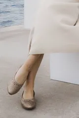 Zapato plano tipo chata, color bronce metalizado, con capellada y forro de cuero vacuno trenzado a mano. Posee un taco bajo de 2,5 cm.