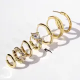 Par de aros tipo argolla dorados con bisagra, con un cristal en forma de corazón y pequeños cristales alrededor.