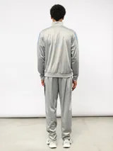 Conjunto deportivo Umbro compuesto por campera de cuello alto con cierre frontal y pantalón de corte recto. La campera presenta bloques de color blanco en los hombros y el logo de la marca bordado en el pecho. Confeccionado en tejido sintético con acabado satinado.