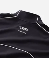 Buzo deportivo de corte boxy, color negro, con cuello alto, cierre frontal completo y mangas largas. Presenta detalles de líneas blancas a lo largo de las mangas y lettering estampado en el pecho.