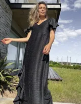 Vestido largo de lurex negro con acabado brillante, escote en V, mangas cortas con volados y falda con tajo lateral que revela un forro interior.