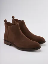 Bota Chelsea de gamuza gris con elásticos laterales, suela de goma marrón y tirador trasero.